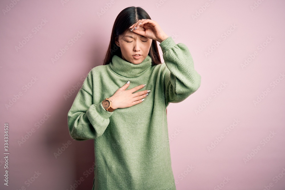 Young beautiful asian woman wearing green winter sweater over pink solated background Touching forehead for illness and fever, flu and cold, virus sick Young beautiful asian woman wearing green winter sweater over pink solated background Touching forehead for illness and fever, flu and cold, virus sick