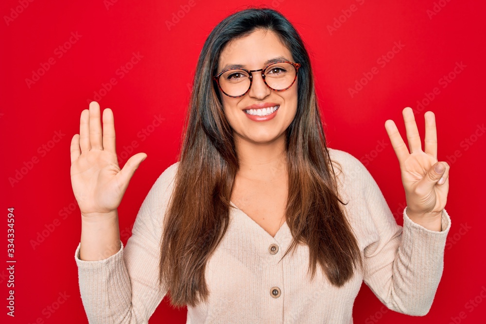 Young hispanic smart woman wearing glasses standing over red isolated background showing and pointing up with fingers number eight while smiling confident and happy. Young hispanic smart woman wearing glasses standing over red isolated background showing and pointing up with fingers number eight while smiling confident and happy.