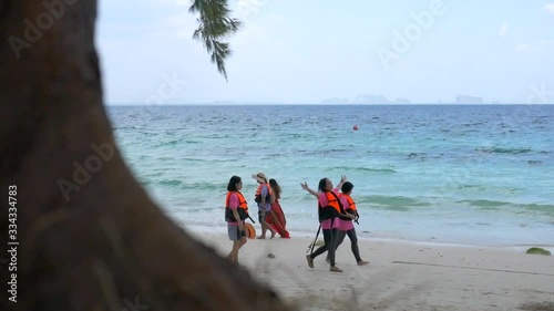 Look through the tree see group tourists enjoy and relaxing by the blue sea and cloud sky. At tropical beach in Thailand. photo
