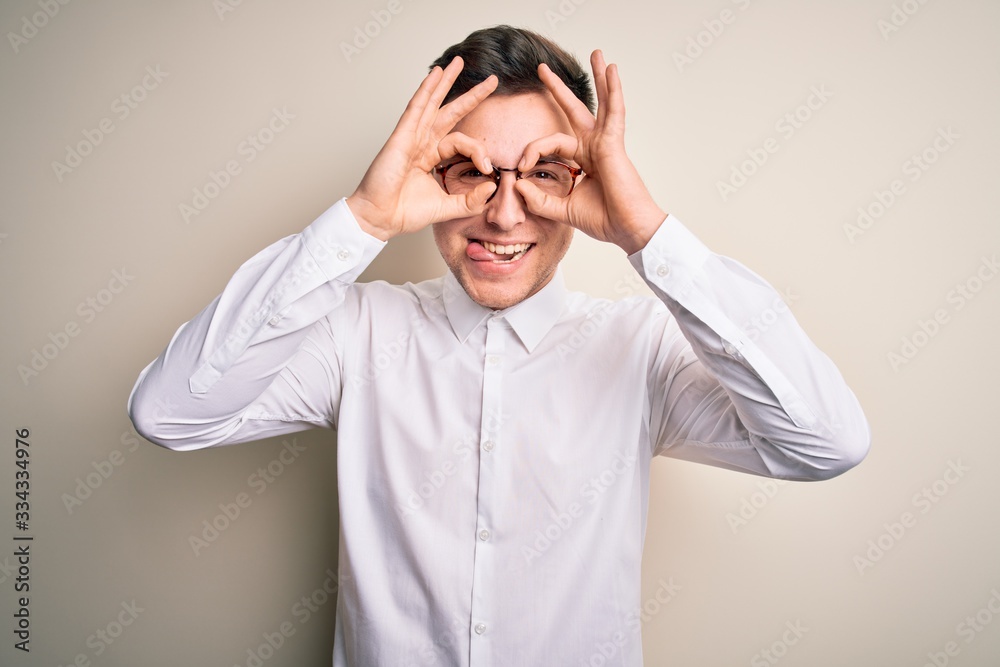 Young handsome business mas wearing glasses and elegant shirt over isolated background doing ok gesture like binoculars sticking tongue out, eyes looking through fingers. Crazy expression. Young handsome business mas wearing glasses and elegant shirt over isolated background doing ok gesture like binoculars sticking tongue out, eyes looking through fingers. Crazy expression.
