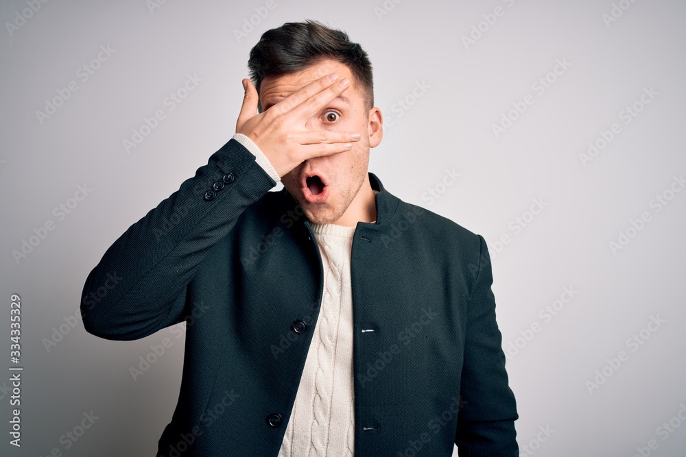 Young handsome business mas wearing elegant winter coat standing over isolated background peeking in shock covering face and eyes with hand, looking through fingers with embarrassed expression. Young handsome business mas wearing elegant winter coat standing over isolated background peeking in shock covering face and eyes with hand, looking through fingers with embarrassed expression.
