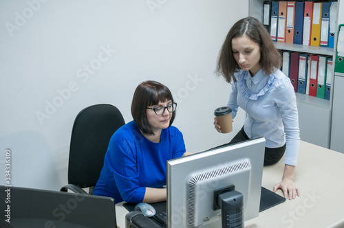 Office, a woman in a blue dress and a brunette girl working on a computer together