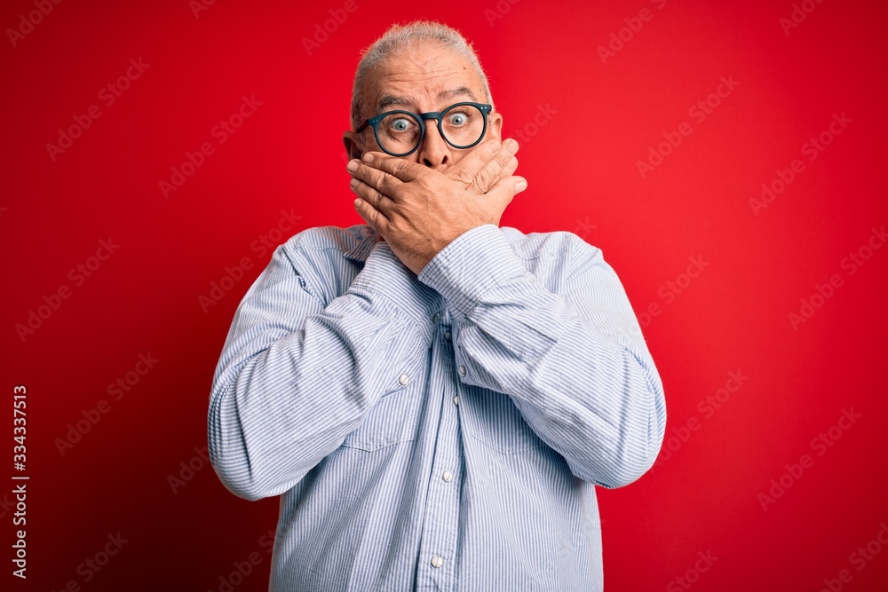 Middle age handsome hoary man wearing casual striped shirt and glasses over red background shocked covering mouth with hands for mistake. Secret concept. Middle age handsome hoary man wearing casual striped shirt and glasses over red background shocked covering mouth with hands for mistake. Secret concept.
