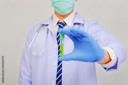 Medical doctor in white uniform doctor wears medical gloves, medical masks and and wearing protective glasses holding blood tube on gray background, corona virus concept, medical concept photo