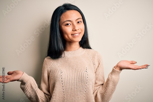 Young beautiful chinese woman wearing casual sweater over isolated white background smiling showing both hands open palms, presenting and advertising comparison and balance