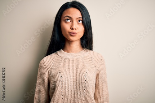 Young beautiful chinese woman wearing casual sweater over isolated white background making fish face with lips, crazy and comical gesture. Funny expression. © Krakenimages.com
