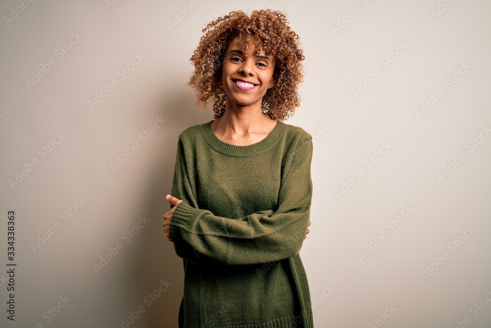 Beautiful african american woman with curly hair wearing casual sweater over white background happy face smiling with crossed arms looking at the camera. Positive person. Beautiful african american woman with curly hair wearing casual sweater over white background happy face smiling with crossed arms looking at the camera. Positive person.