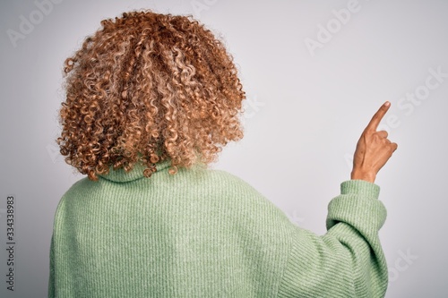 Young beautiful african american woman wearing turtleneck sweater and glasses Posing backwards pointing ahead with finger hand