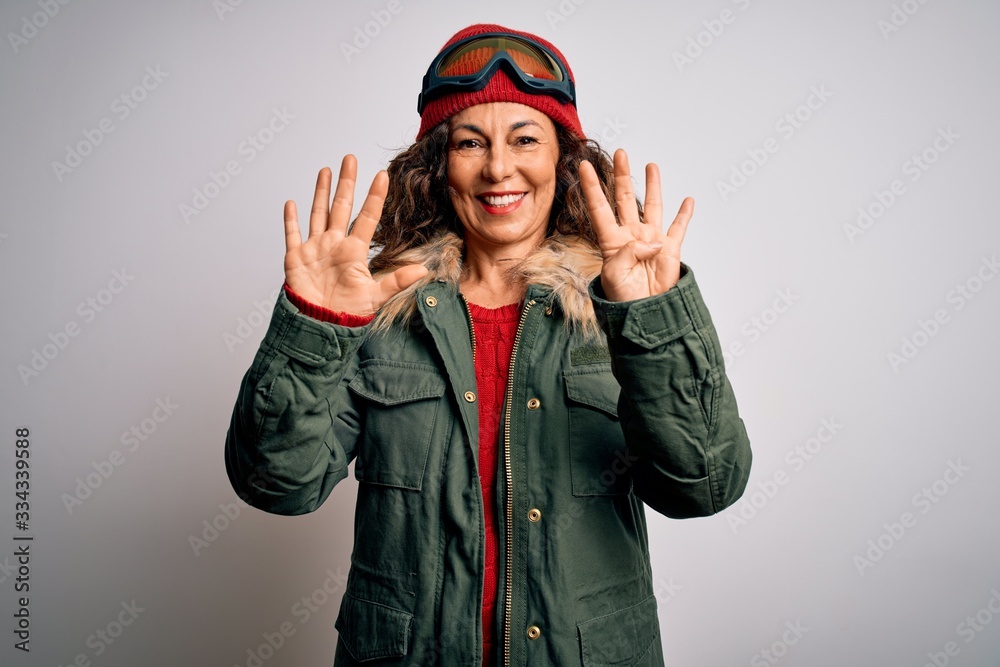 Fototapeta premium Middle age skier woman wearing snow sportswear and ski goggles over white background showing and pointing up with fingers number nine while smiling confident and happy.
