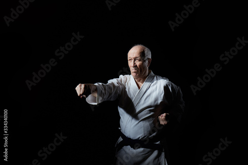 Old athlete performs punches on a black background