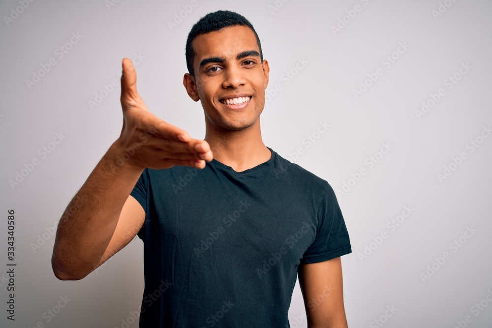 Young handsome african american man wearing casual t-shirt standing over white background smiling friendly offering handshake as greeting and welcoming. Successful business. Young handsome african american man wearing casual t-shirt standing over white background smiling friendly offering handshake as greeting and welcoming. Successful business.