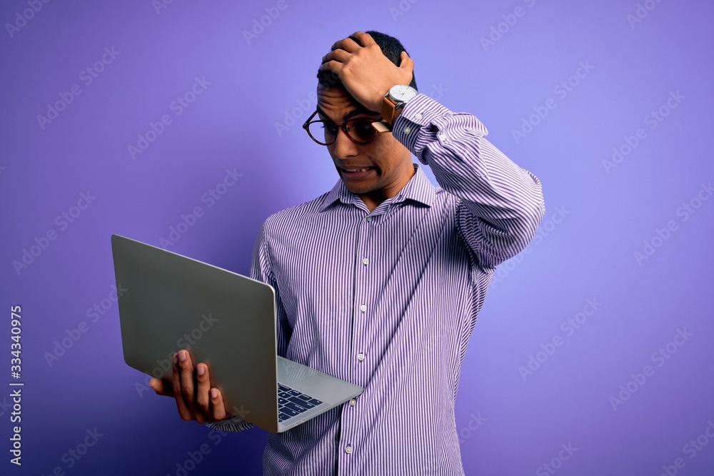 Young handsome african american business man working using laptop over purple background stressed with hand on head, shocked with shame and surprise face, angry and frustrated. Fear and upset