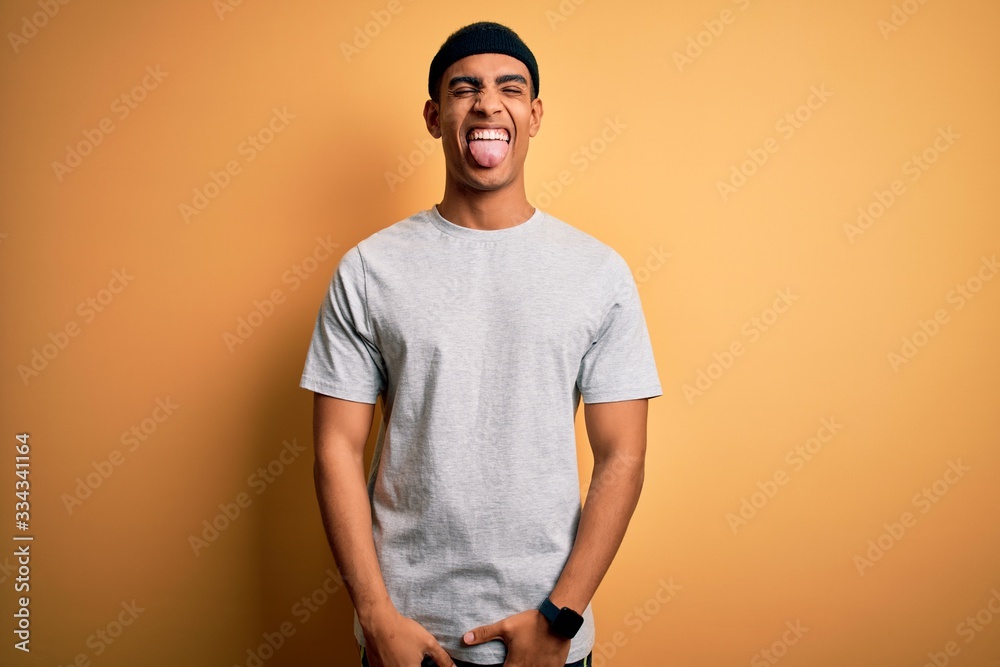 Handsome african american sportsman doing sport wearing sportswear over yellow background sticking tongue out happy with funny expression. Emotion concept. Handsome african american sportsman doing sport wearing sportswear over yellow background sticking tongue out happy with funny expression. Emotion concept.
