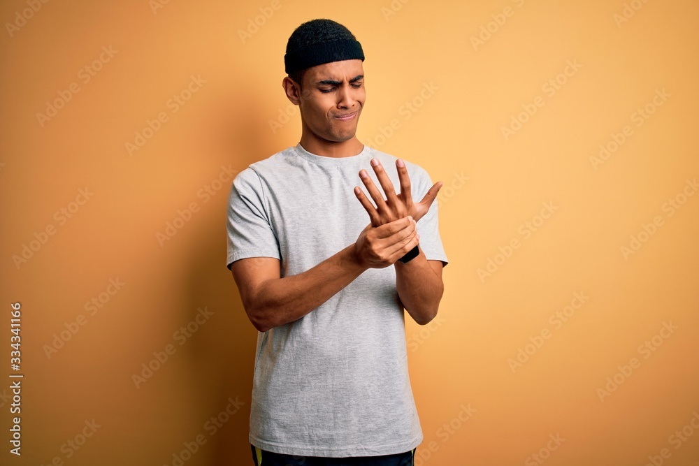 Handsome african american sportsman doing sport wearing sportswear over yellow background Suffering pain on hands and fingers, arthritis inflammation Handsome african american sportsman doing sport wearing sportswear over yellow background Suffering pain on hands and fingers, arthritis inflammation