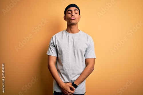 Handsome african american sportsman doing sport wearing sportswear over yellow background looking at the camera blowing a kiss on air being lovely and sexy. Love expression. © Krakenimages.com