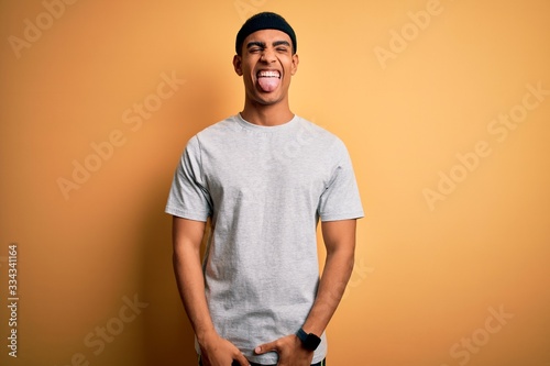 Handsome african american sportsman doing sport wearing sportswear over yellow background sticking tongue out happy with funny expression. Emotion concept. © Krakenimages.com