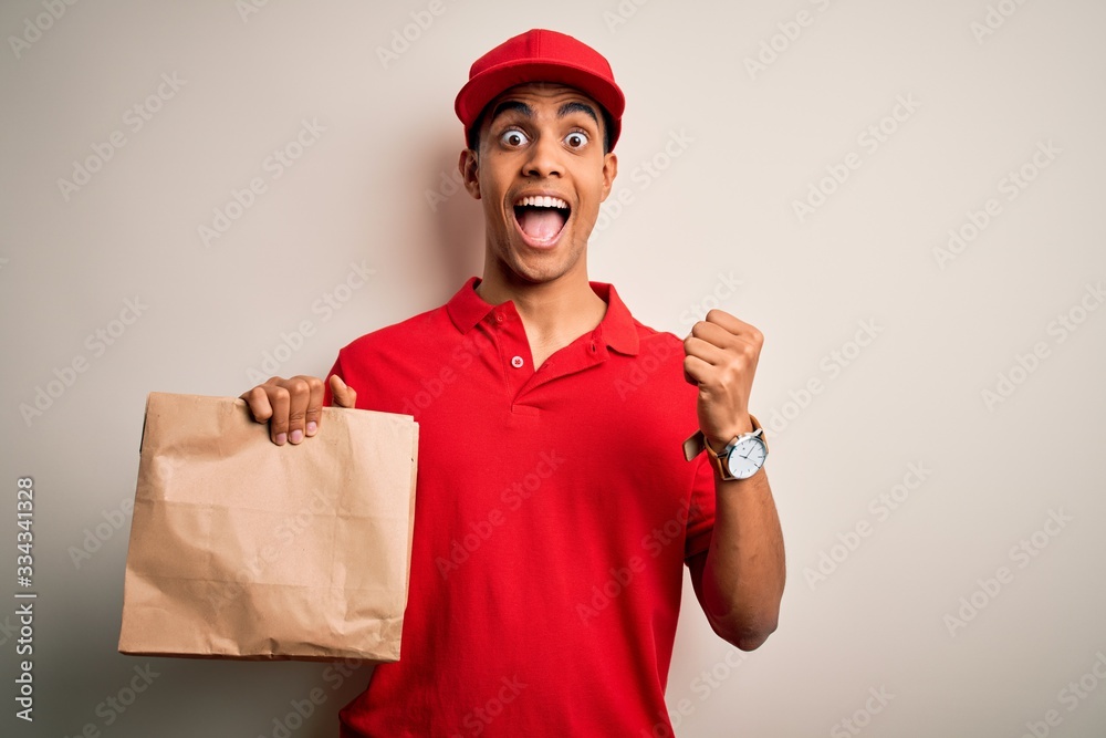 Young handsome african american delivery man holding paper bag with takeaway food screaming proud and celebrating victory and success very excited, cheering emotion