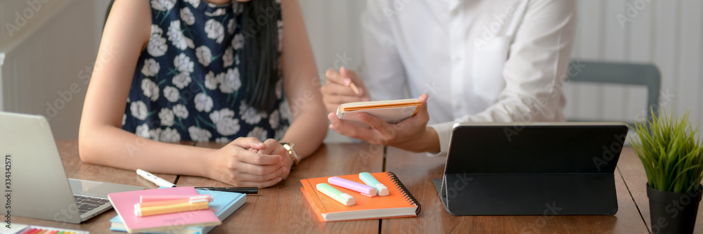 Cropped shot of two university students consulting on their thesis on wooden table Cropped shot of two university students consulting on their thesis on wooden table