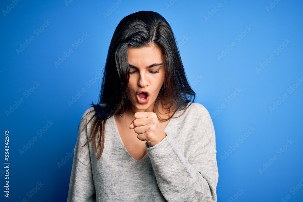 Young beautiful brunette woman wearing casual sweater standing over blue background feeling unwell and coughing as symptom for cold or bronchitis. Health care concept. Young beautiful brunette woman wearing casual sweater standing over blue background feeling unwell and coughing as symptom for cold or bronchitis. Health care concept.