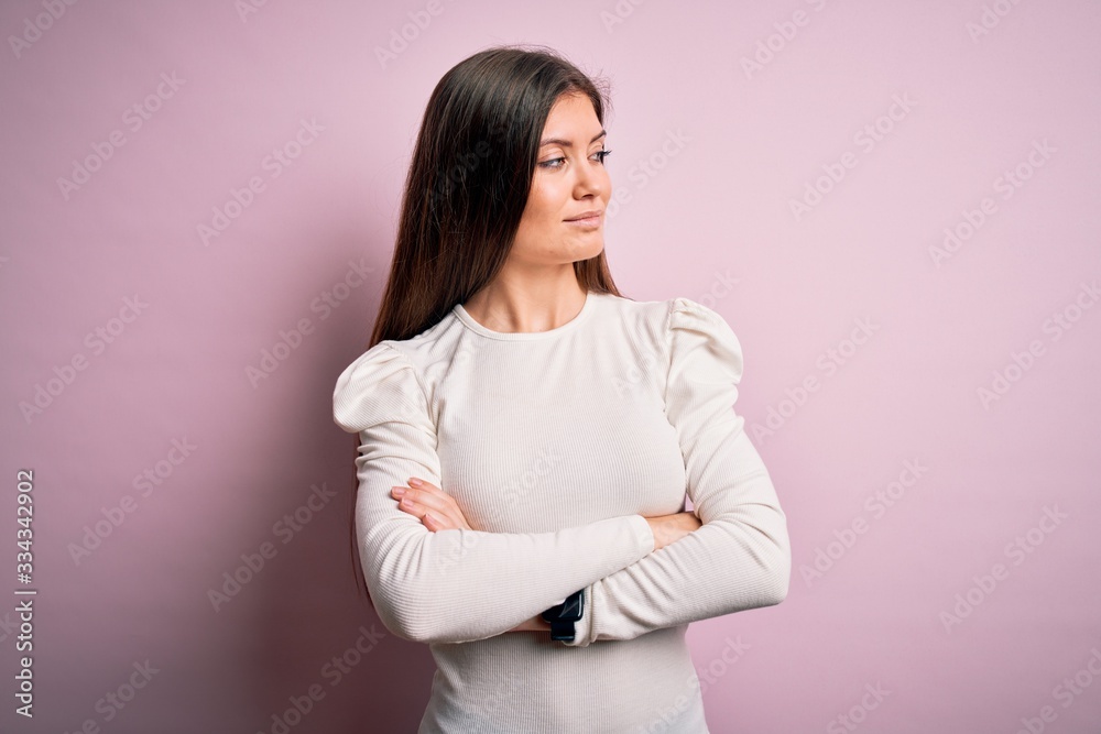 Young beautiful woman with blue eyes wearing casual white t-shirt over pink background looking to the side with arms crossed convinced and confident Young beautiful woman with blue eyes wearing casual white t-shirt over pink background looking to the side with arms crossed convinced and confident