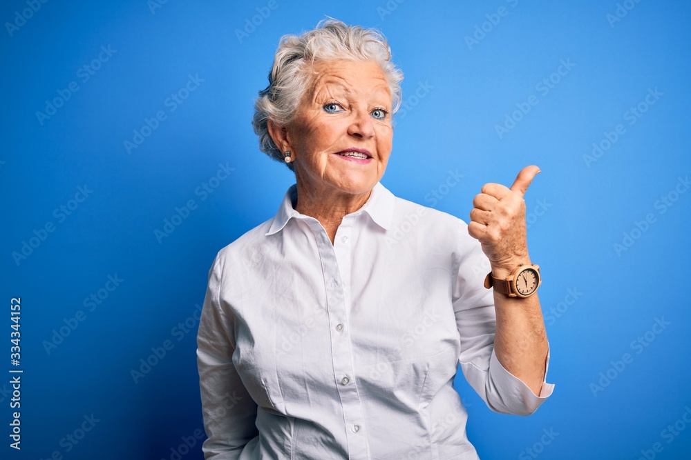 Φωτογραφία Senior beautiful woman wearing elegant shirt standing over isolated blue background smiling with happy face looking and pointing to the side with thumb up