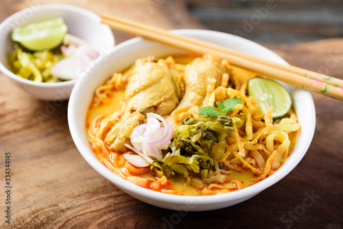 Traditional Northern Thai food (Khao Soi), spicy curry noodles soup with coconut milk and chicken in a bowl on wooden background