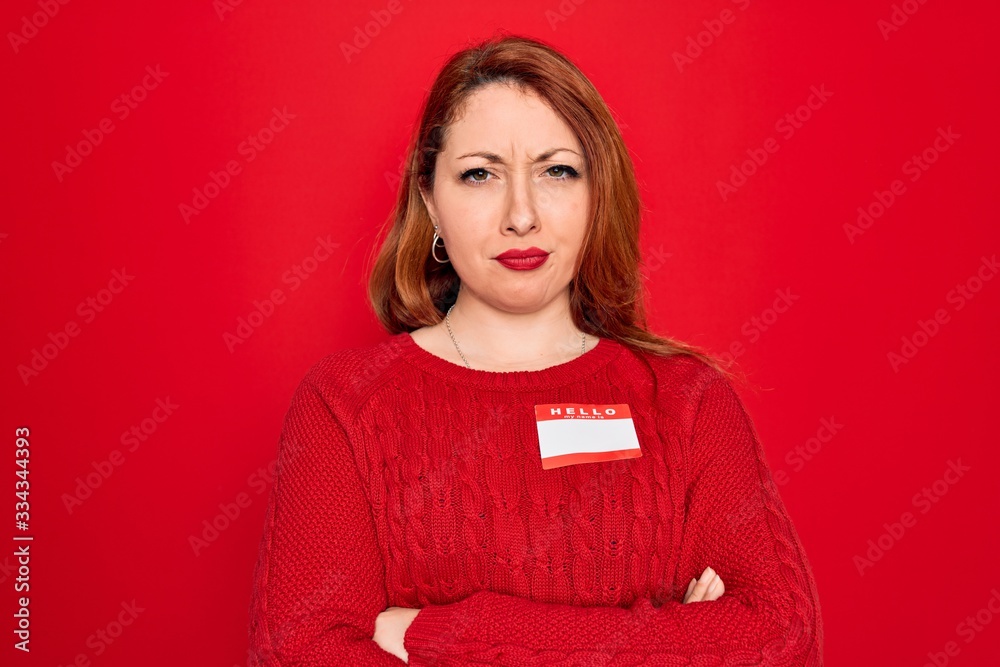 Young beautiful redhead woman wearing sticker presentation with hello my name message skeptic and nervous, disapproving expression on face with crossed arms. Negative person. Young beautiful redhead woman wearing sticker presentation with hello my name message skeptic and nervous, disapproving expression on face with crossed arms. Negative person.
