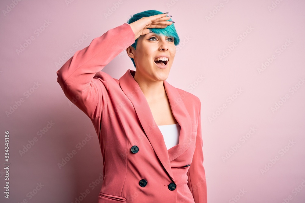 Young beautiful businesswoman with blue fashion hair wearing jacket over pink background very happy and smiling looking far away with hand over head. Searching concept. Young beautiful businesswoman with blue fashion hair wearing jacket over pink background very happy and smiling looking far away with hand over head. Searching concept.