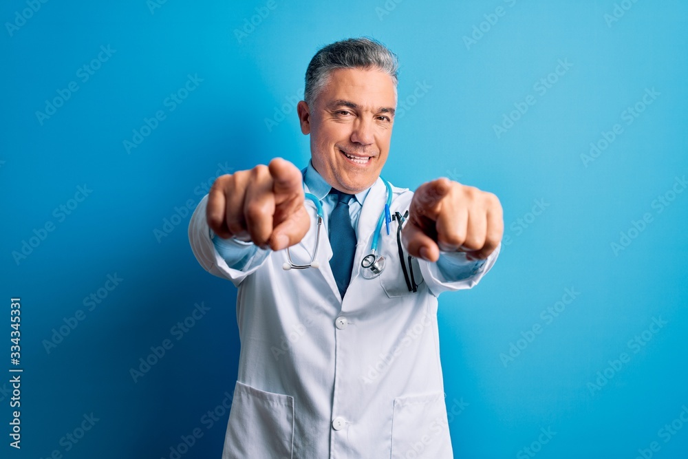 Middle age handsome grey-haired doctor man wearing coat and blue stethoscope pointing to you and the camera with fingers, smiling positive and cheerful Middle age handsome grey-haired doctor man wearing coat and blue stethoscope pointing to you and the camera with fingers, smiling positive and cheerful