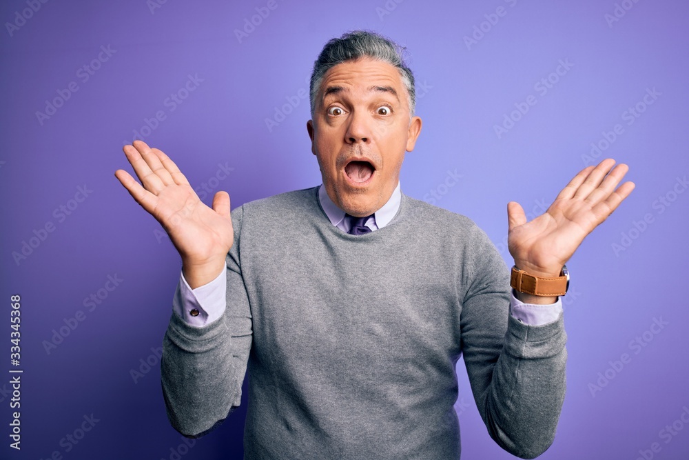 Fototapeta premium Middle age handsome grey-haired man wearing elegant sweater over purple background celebrating crazy and amazed for success with arms raised and open eyes screaming excited. Winner concept