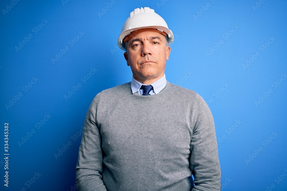 Middle age handsome grey-haired engineer man wearing safety helmet over blue background Relaxed with serious expression on face. Simple and natural looking at the camera. Middle age handsome grey-haired engineer man wearing safety helmet over blue background Relaxed with serious expression on face. Simple and natural looking at the camera.