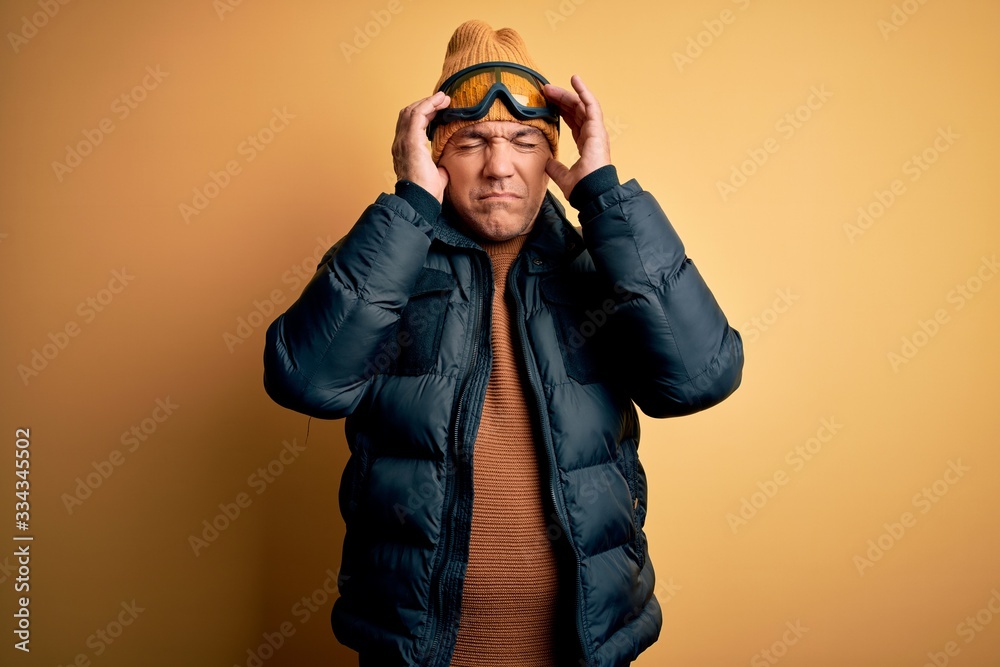 Middle age handsome grey-haired skier man on vacation wearing ski goggles with hand on head for pain in head because stress. Suffering migraine. Middle age handsome grey-haired skier man on vacation wearing ski goggles with hand on head for pain in head because stress. Suffering migraine.