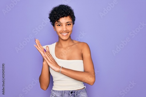 Young beautiful african american afro woman wearing casual t-shirt over purple background clapping and applauding happy and joyful, smiling proud hands together