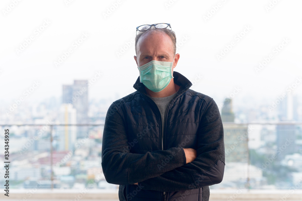 Mature man wearing mask with arms crossed against view of the city