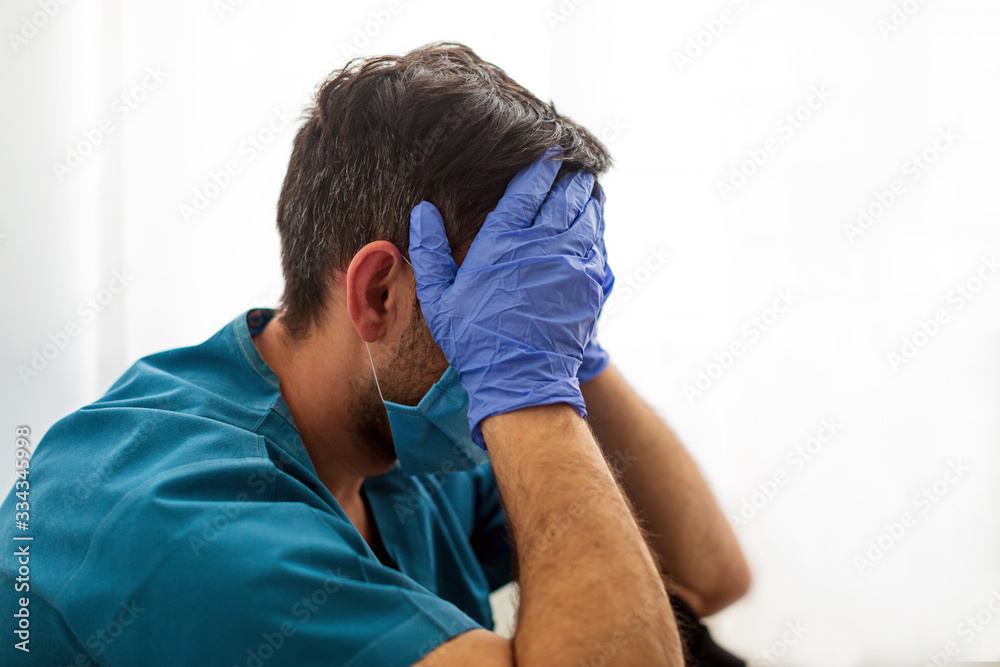 Φωτογραφία Tired young doctor from lack of sleep sits near the window covering his face with his hands