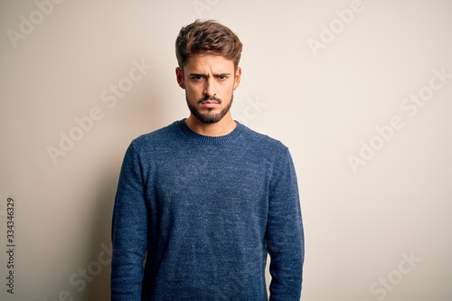 Young handsome man with beard wearing casual sweater standing over white background skeptic and nervous, frowning upset because of problem. Negative person.