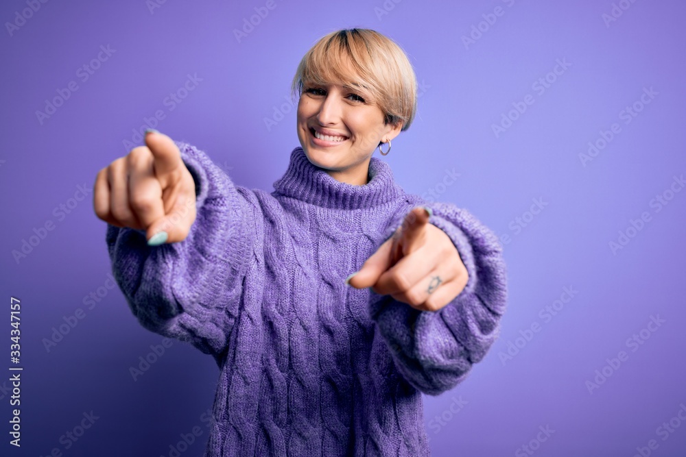 Young blonde woman with short hair wearing winter turtleneck sweater over purple background pointing to you and the camera with fingers, smiling positive and cheerful Young blonde woman with short hair wearing winter turtleneck sweater over purple background pointing to you and the camera with fingers, smiling positive and cheerful