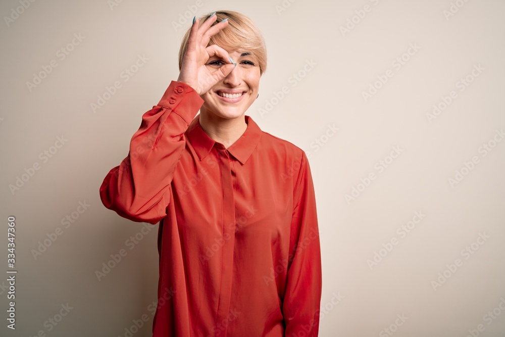 Young beautiful business blonde woman with short hair standing over isolated background doing ok gesture with hand smiling, eye looking through fingers with happy face. Young beautiful business blonde woman with short hair standing over isolated background doing ok gesture with hand smiling, eye looking through fingers with happy face.