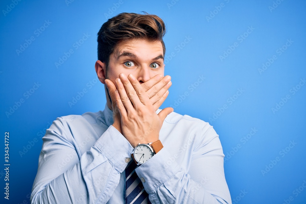 Young blond businessman with beard and blue eyes wearing elegant shirt and tie standing shocked covering mouth with hands for mistake. Secret concept. Young blond businessman with beard and blue eyes wearing elegant shirt and tie standing shocked covering mouth with hands for mistake. Secret concept.