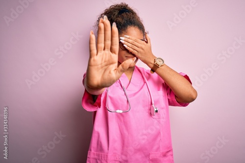 African american nurse girl wearing medical uniform and stethoscope over pink background covering eyes with hands and doing stop gesture with sad and fear expression. Embarrassed and negative concept.