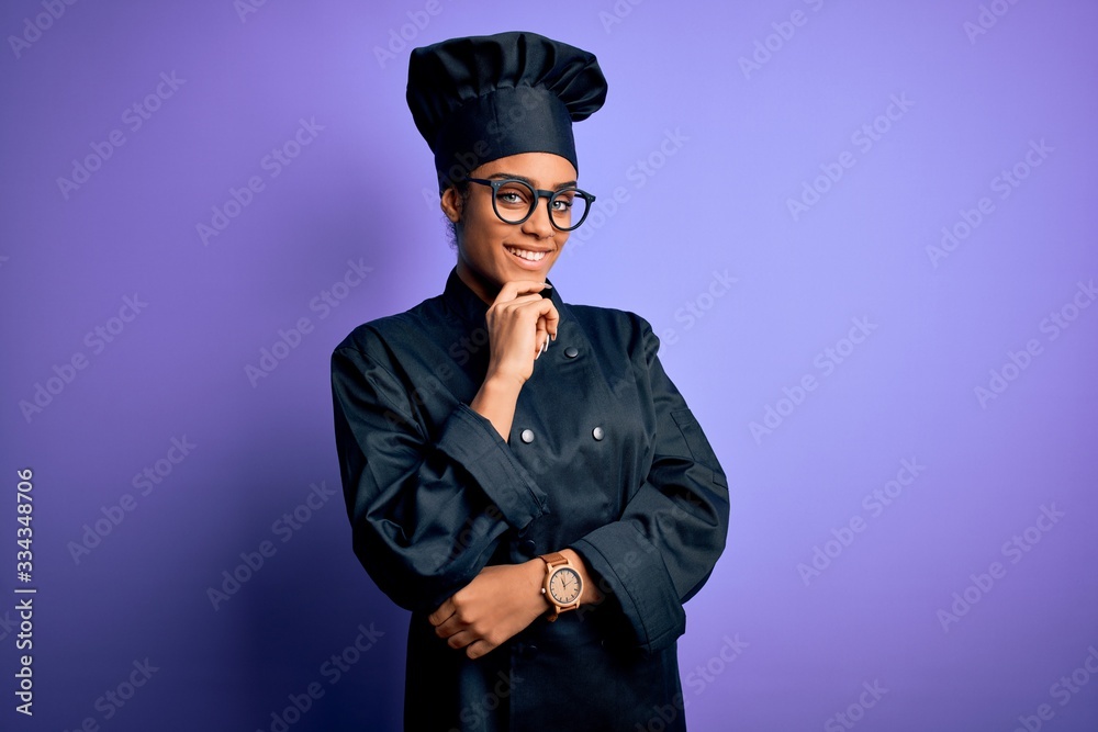 Young african american chef girl wearing cooker uniform and hat over purple background looking confident at the camera smiling with crossed arms and hand raised on chin. Thinking positive. Young african american chef girl wearing cooker uniform and hat over purple background looking confident at the camera smiling with crossed arms and hand raised on chin. Thinking positive.