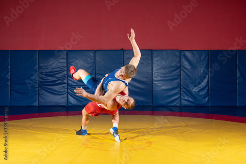Two greco-roman  wrestlers in red and blue uniform wrestling  on a yellow wrestling carpet in the gym