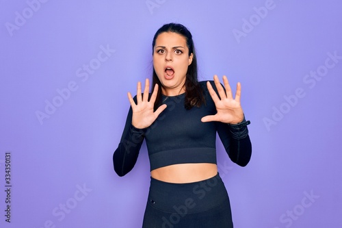 Young beautiful brunette sporty woman wearing casual sportswear over purple background afraid and terrified with fear expression stop gesture with hands, shouting in shock. Panic concept.