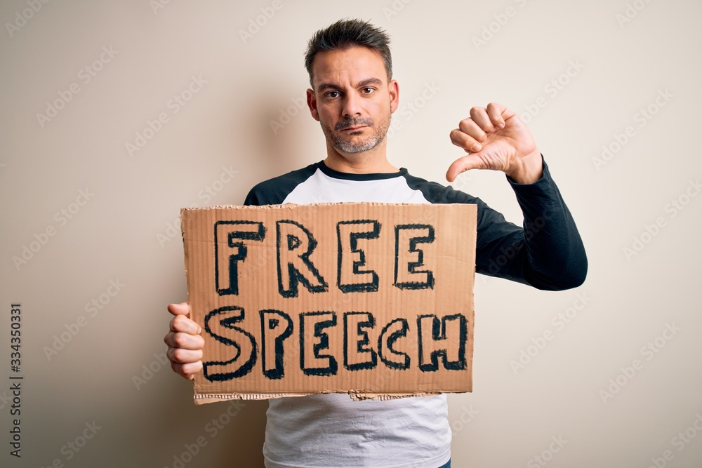 Young handsome man asking for rights holding banner with free speech message with angry face, negative sign showing dislike with thumbs down, rejection concept Young handsome man asking for rights holding banner with free speech message with angry face, negative sign showing dislike with thumbs down, rejection concept