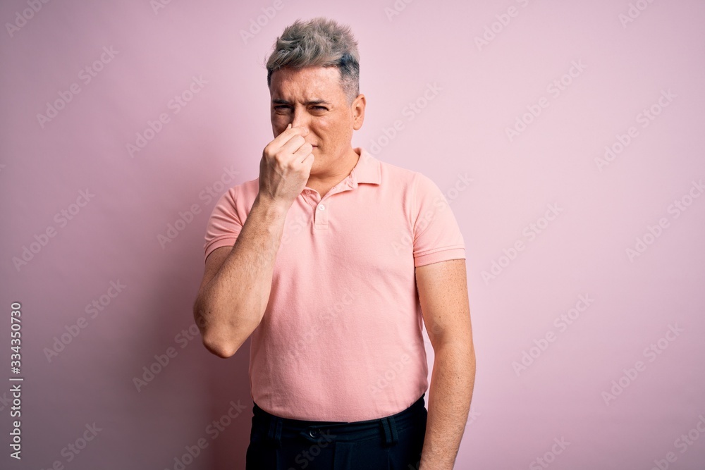 Young handsome modern man wearing casual pink t-shirt over isolated background smelling something stinky and disgusting, intolerable smell, holding breath with fingers on nose. Bad smell Young handsome modern man wearing casual pink t-shirt over isolated background smelling something stinky and disgusting, intolerable smell, holding breath with fingers on nose. Bad smell