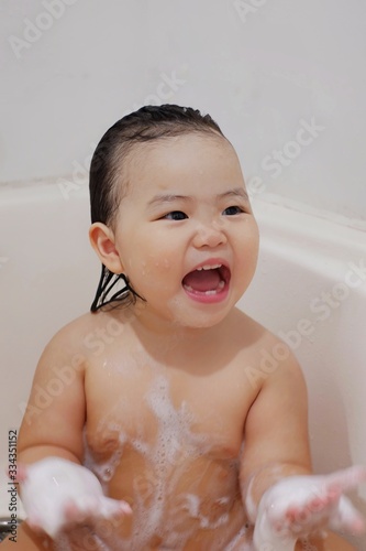 A cute Asian girl playing a yellow rubber ducky in a bathtub, happy, laughing and smiling.