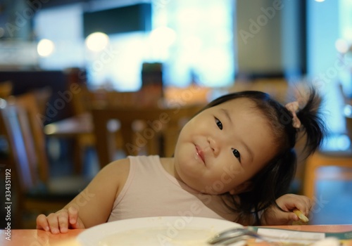 Quadro em tela A cute Asian girl eating salad at a restaurant with her mom feeding her using fork and spoon