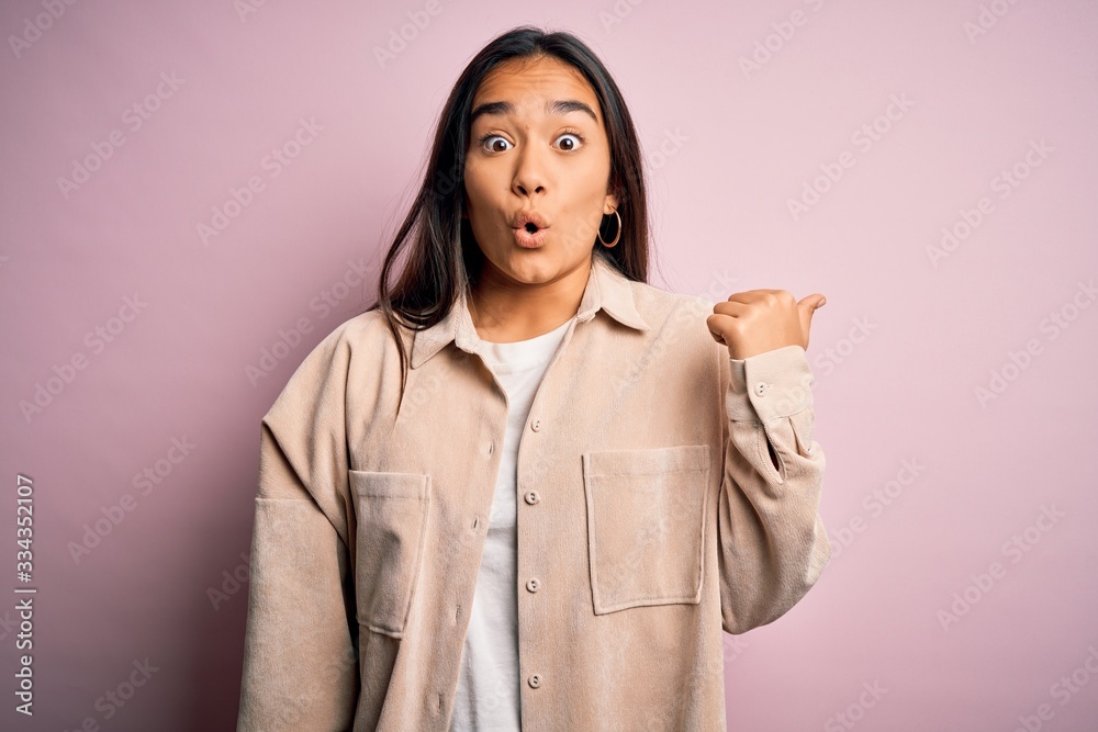Young beautiful asian woman wearing casual shirt standing over pink background Surprised pointing with hand finger to the side, open mouth amazed expression. Young beautiful asian woman wearing casual shirt standing over pink background Surprised pointing with hand finger to the side, open mouth amazed expression.