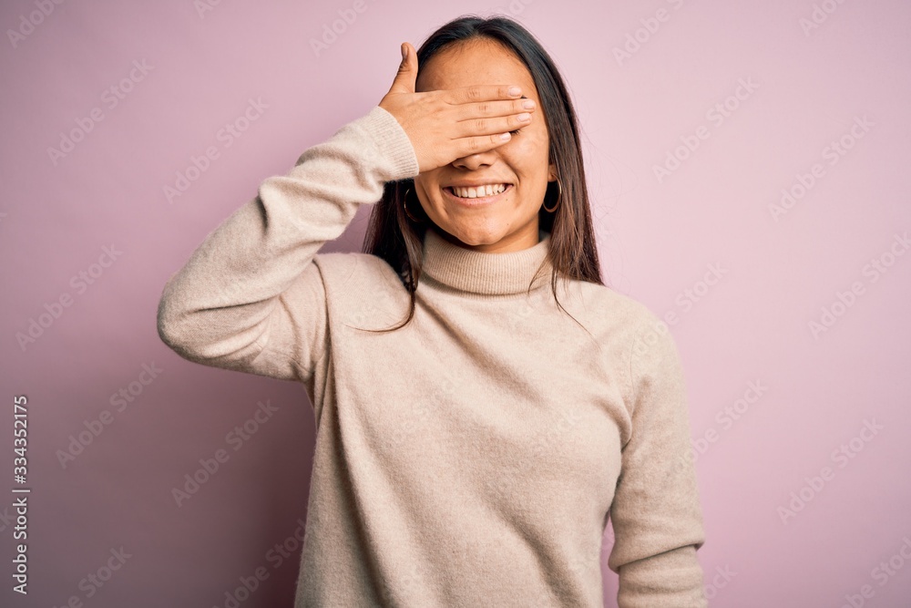 Young beautiful asian woman wearing casual turtleneck sweater over pink background smiling and laughing with hand on face covering eyes for surprise. Blind concept. Young beautiful asian woman wearing casual turtleneck sweater over pink background smiling and laughing with hand on face covering eyes for surprise. Blind concept.