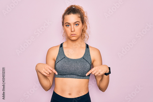 Young beautiful blonde sportswoman with blue eyes doing exercise wearing sportswear Pointing down looking sad and upset, indicating direction with fingers, unhappy and depressed. © Krakenimages.com